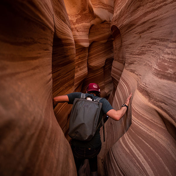 A hiker squeezes through a slot canyon in Grand Staircase-Escalante National Monument
