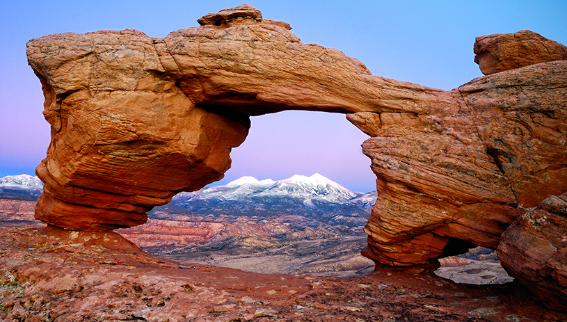 A snowy mountain peeks through the sandstone arch