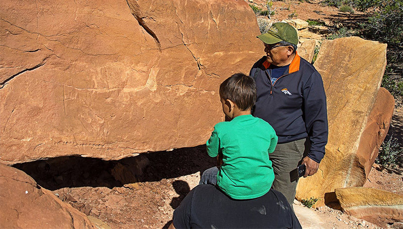 A person points out a petroglyph to a young child.