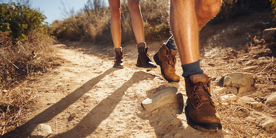 Close-up of legs of young hikers walking on the country path. Young couple trail waking. Focus on hiking shoes.