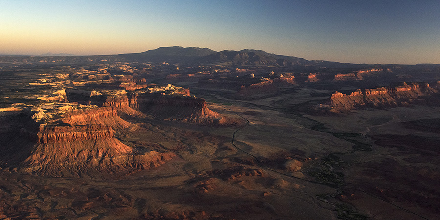 Red canyon and table lands with Indian creek winding down the bottom and the Abajo mountains purple on the horizon
