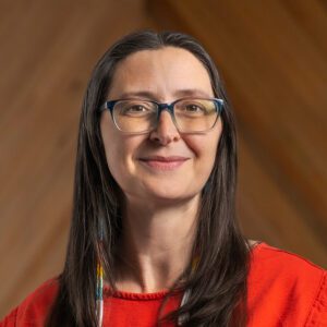 Stephanie Smith, a GIS specialist with long brown hair and glasses, smiles at the camera in a red top against a wooden background.