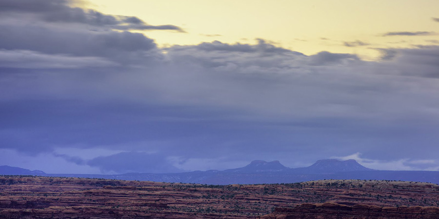 Cloudy sky and the outline of the bears ears buttes, like the ears of a bear peeking up over a band of cliffs