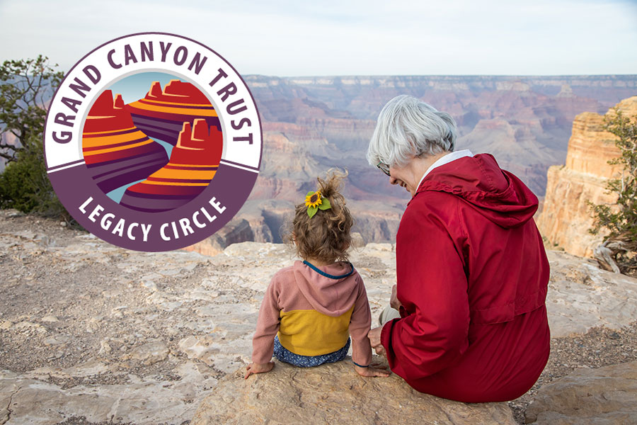A grandma in a red coat sits next to her young granddaughter on the rim of the Grand Canyon