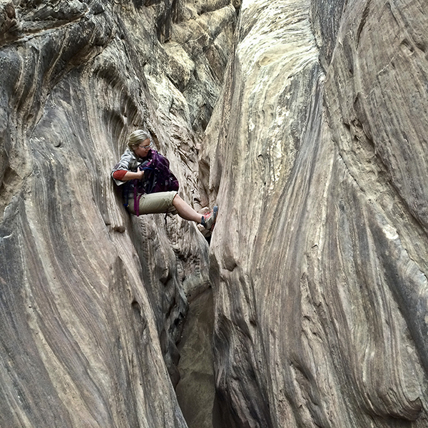 A hiker navigates through a tight slot canyon