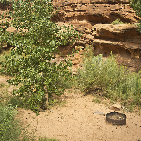 A small sandy campsite with a fire ring up against sandstone cliffs at the Hunter Canyon Campground