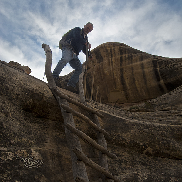 A man starts to climb down a slickrock ledge via a wooden ladder