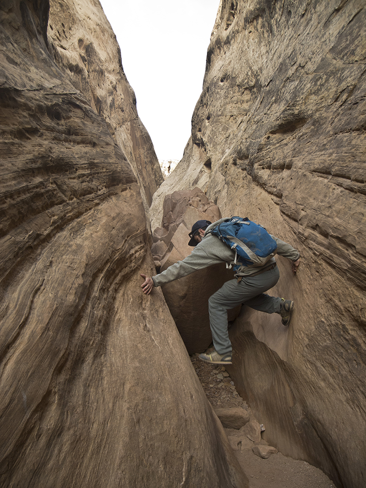 A male hiker pushes off the canyon walls to climb over a chockstone