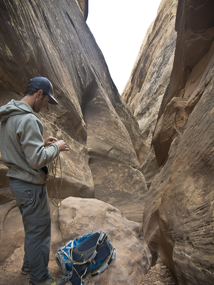 A hiker gets a piece of rope out of his backpack to descend over a chockstone