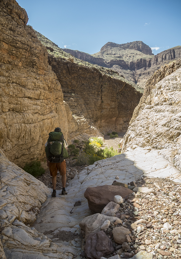 A man with a large backpack descends a tributary canyon in the Grand Canyon