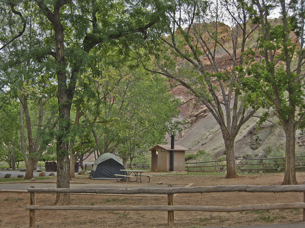 A tent, picnic table, and outhouse behind a wooden fence