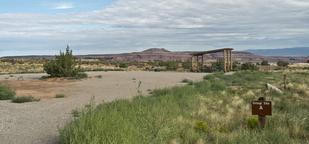 A flat gravel campsite with a shade structure and picnic table underneath