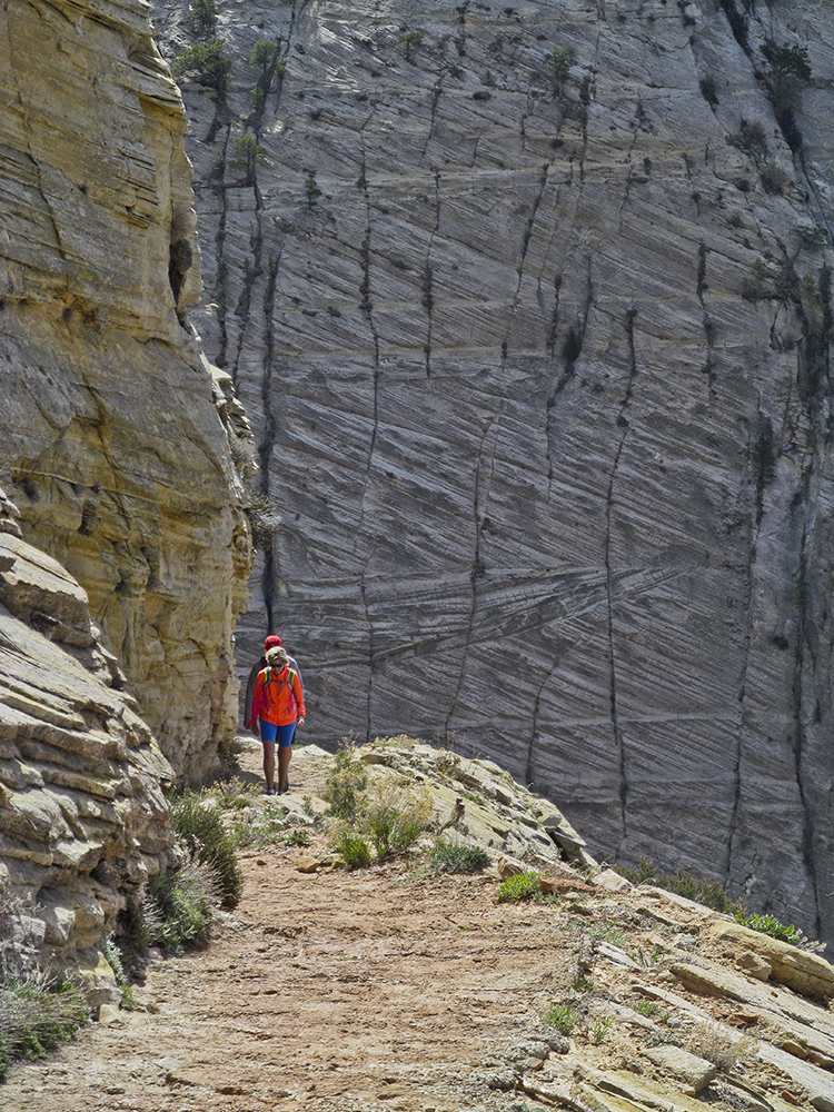 A woman hikes next to steep crossbedded sandstone walls