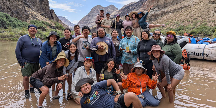 A group of people pose in the shallow waters of the Colorado River during their Grand Canyon River Trip.