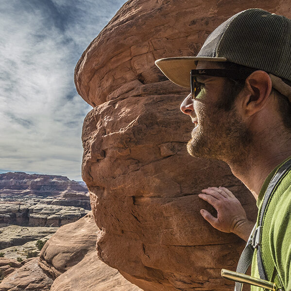 A male hiker looks through a gap in the rocks, onto the large expanse of Canyonlands.