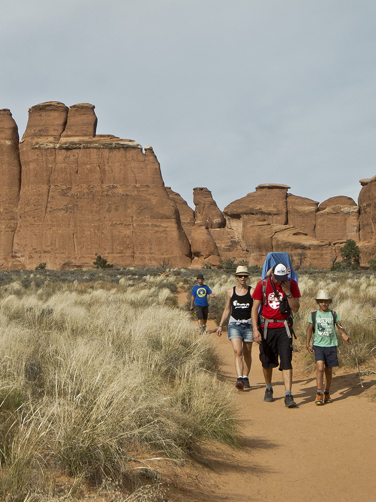 Families hiking on a sandy trail with sandstone spires behind them
