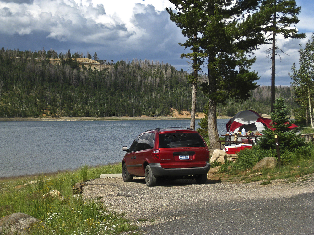 A red minivan parked at a campsite on the shores of Navajo Lake