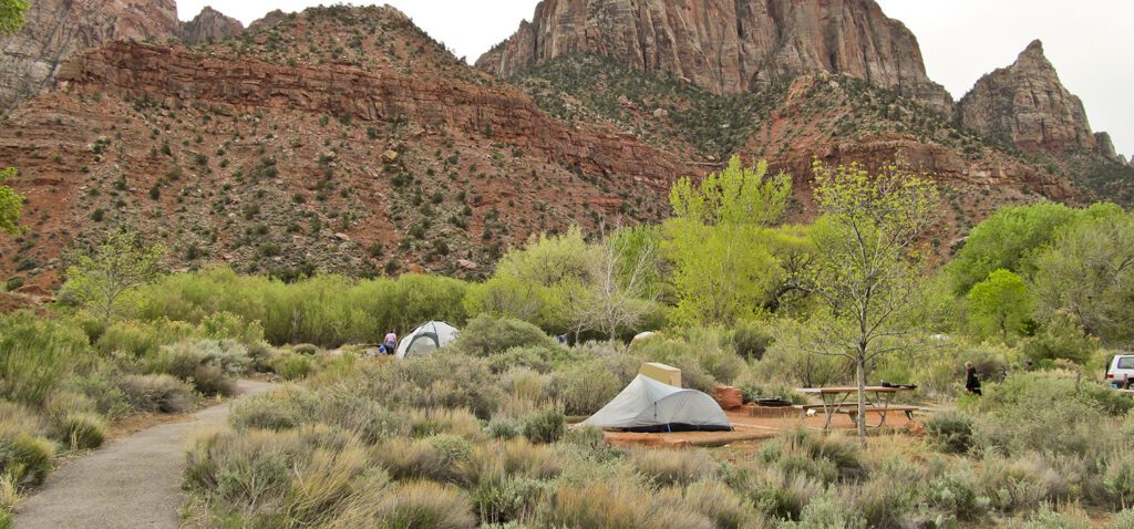 Two tents on gravel tent pads with colorful sandstone cliffs behind them