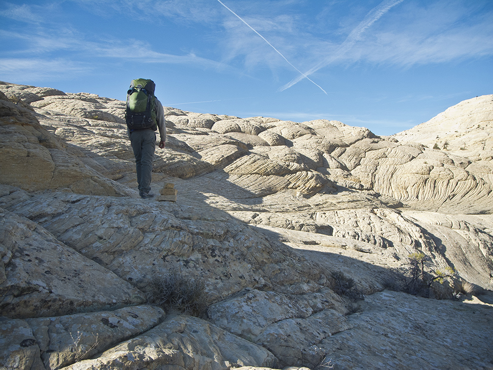 A backpacker crosses pillowy domes of Navajo Sandstone on the Boulder Mail Trail