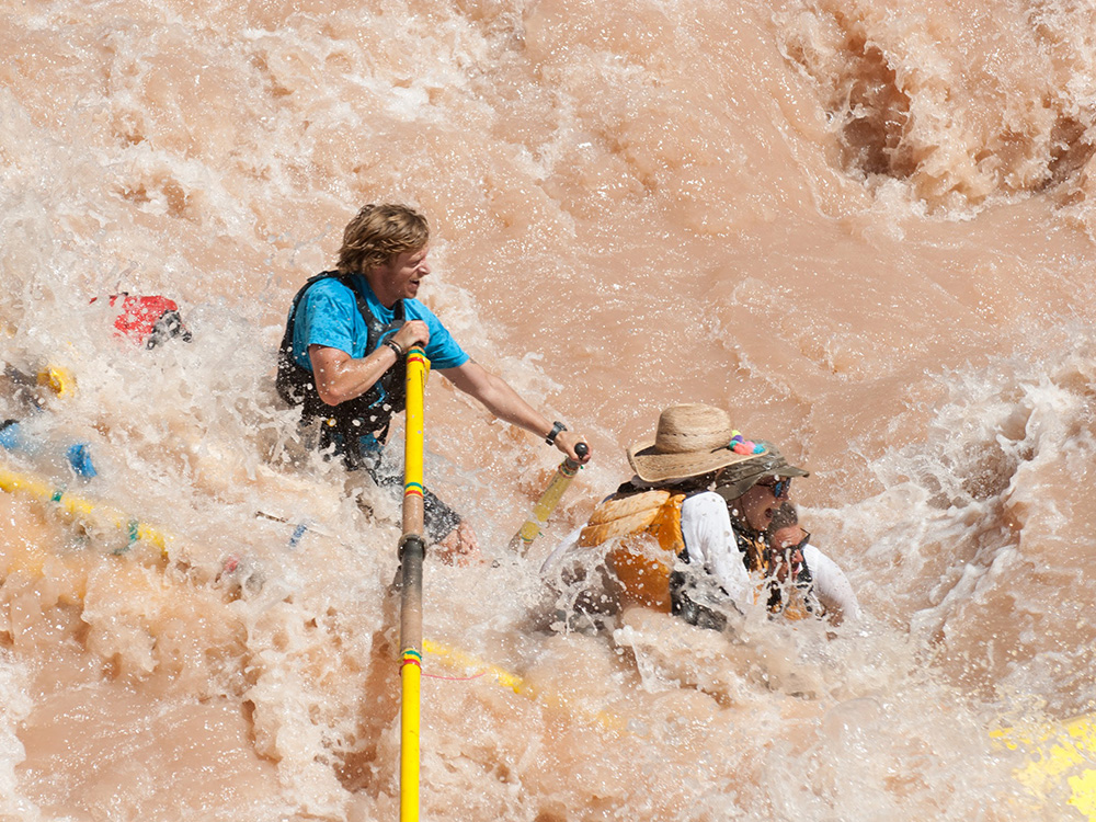 A boatman on an oar raft crashes through the Colorado River's muddy waves