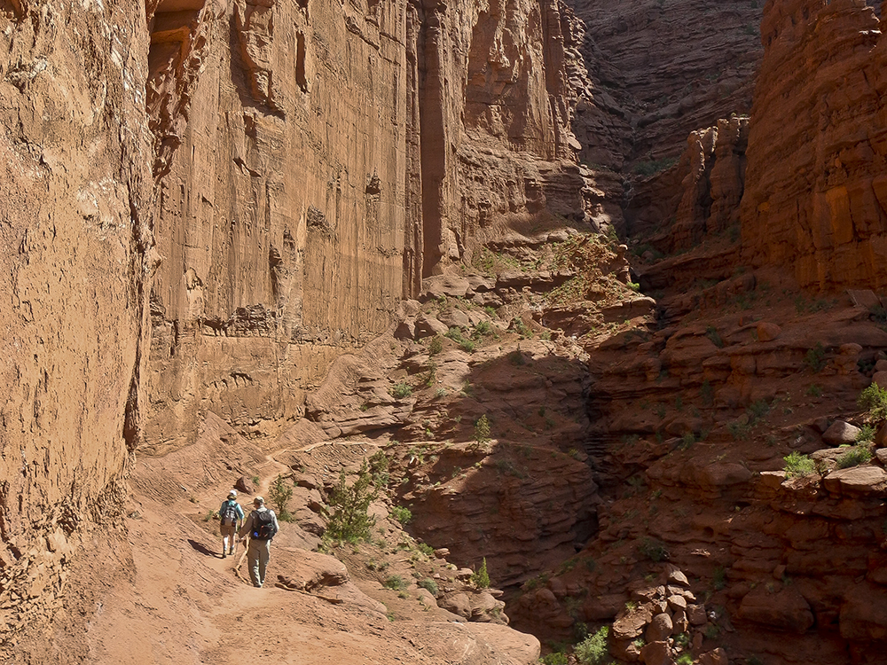 Two hikers on a slickrock bench below the towers