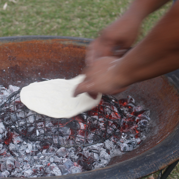 Two hands cooking fry bread on hot coals