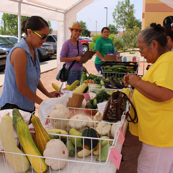 Woman in a yellow shirt examines squashes for sale in a farmer's market
