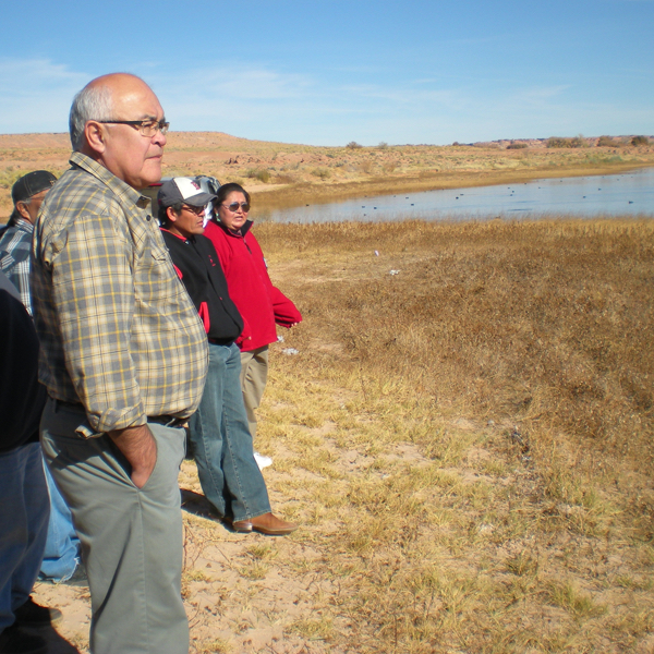 Figures in a brown field with water in the distance