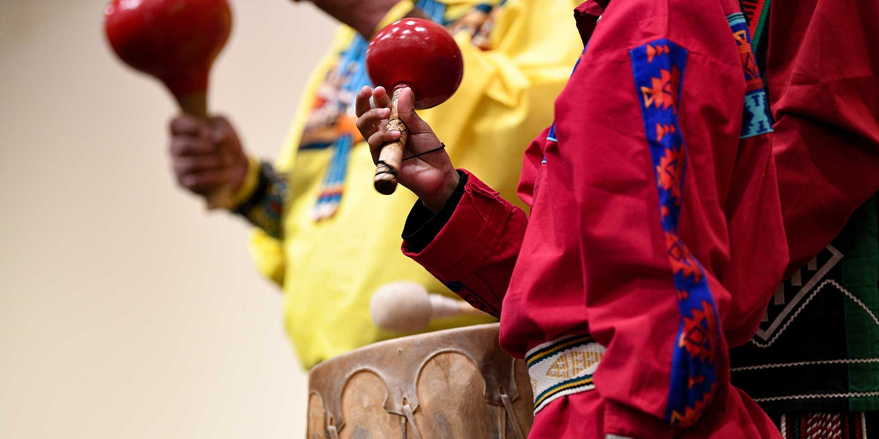 Two figures, one in a red and one in a yellow shirt, play traditional instruments