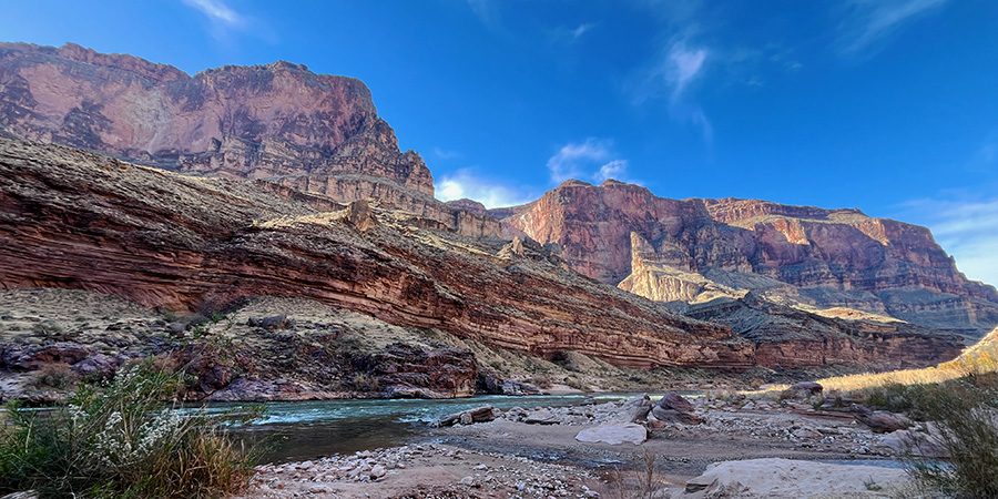 Rocky bank of green Colorado River with pink cliffs rising above.
