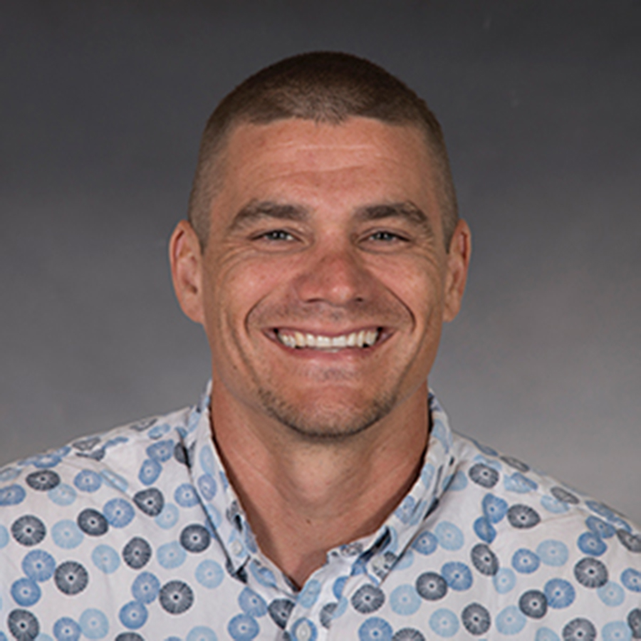Smiling man in a blue and white shit with very close-shaven hair