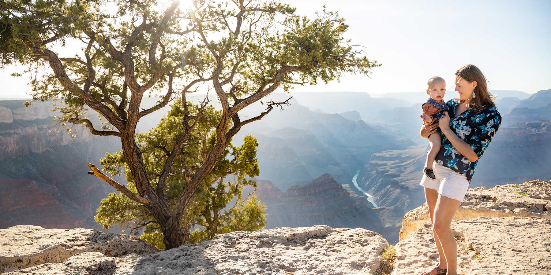 A young mother stands on the rim of the Grand Canyon holding her baby boy.
