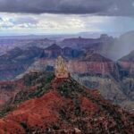 Point Imperial, a whitish chimney of rock on top of bright red rocks, on the North Rim of the Grand Canyon during a monsoon storm, rain and clouds