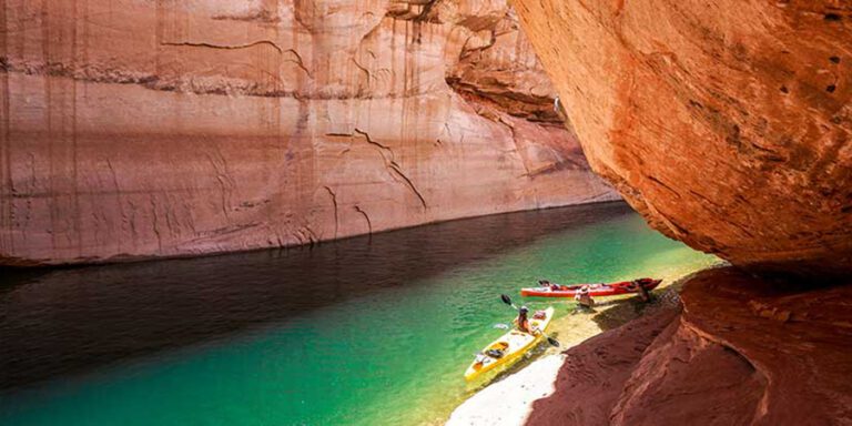 Two kayaks, one yellow and one red, at the edge of red canyon walls on calm green water in Glen Canyon