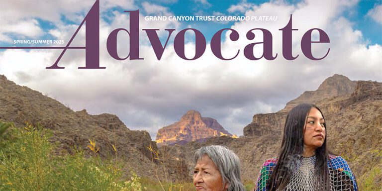 Two women stand outdoors amid rocky canyon scenery under a cloudy sky, with a mountain peak in the background. This is the cover of the 2025 Spring Advocate magazine, capturing adventure and connection in nature.