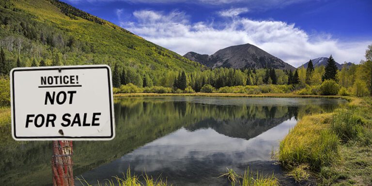 A sign reading "Notice! Not For Sale" stands in front of a small lake, surrounded by trees and mountains under a blue sky with clouds.