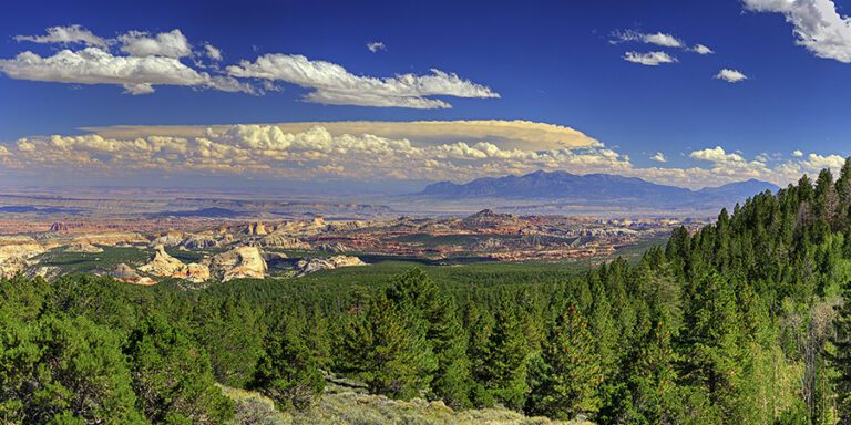 View of a vast forested landscape with rocky outcrops, distant mountains, and a sky filled with scattered clouds.