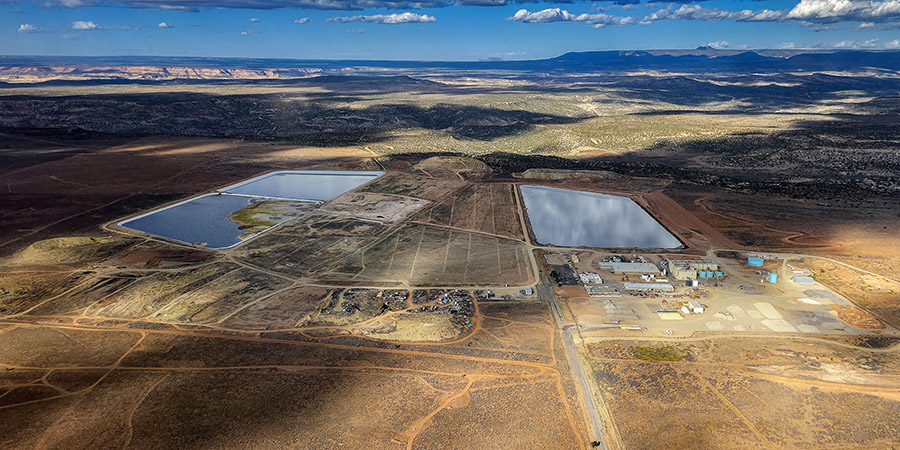 Aerial view of a uranium mill industrial site with two large blue ponds, several buildings, and access roads set in an arid, sparsely vegetated landscape.