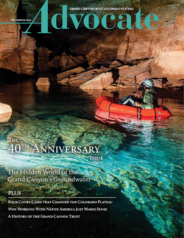 A person in a red inflatable kayak paddles through a clear, blue underground river surrounded by rocky cave walls; cover of Grand Canyon Trust Advocate Magazine.